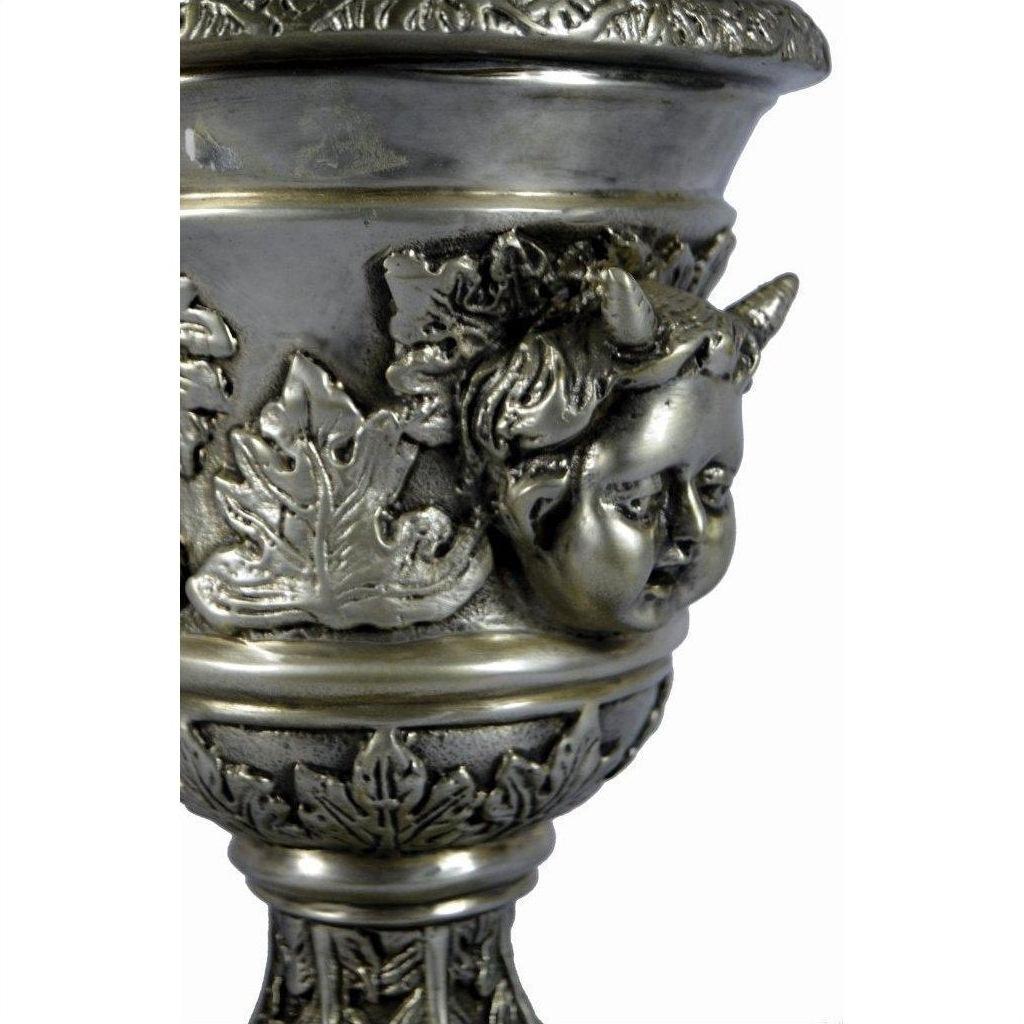 Close-up of a silver plate urn with cherub face and ornate leaf relief designs.