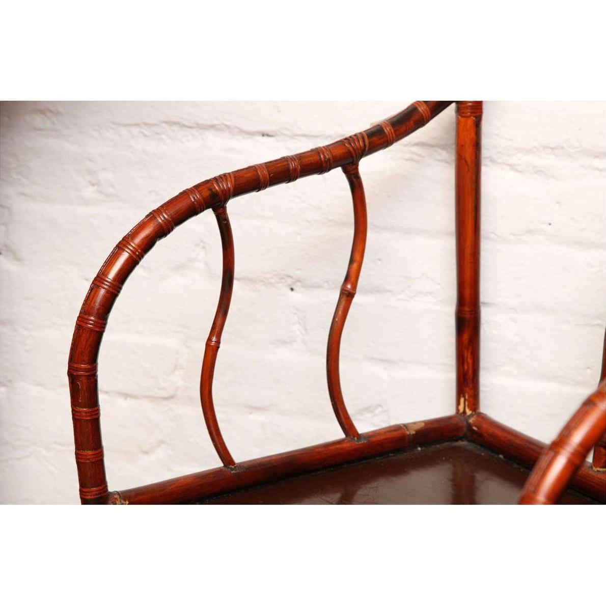Close-up of brown bamboo and elm horseshoe-back armchair, 19th century, indoors against a white brick wall.