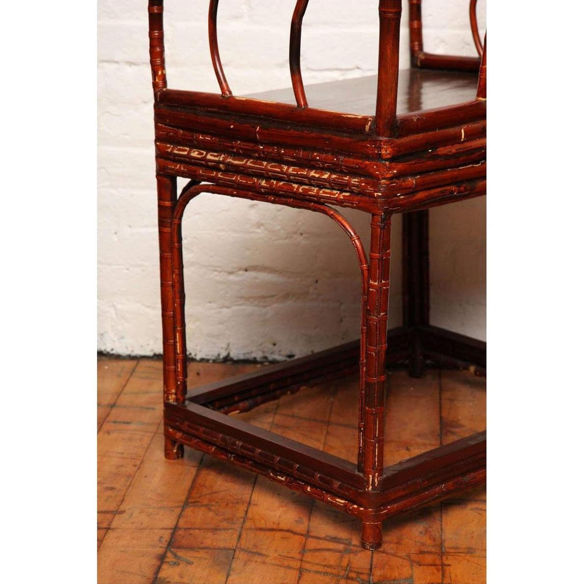 Close-up of brown bamboo and elm horseshoe-back armchair on wood floor against white brick wall.