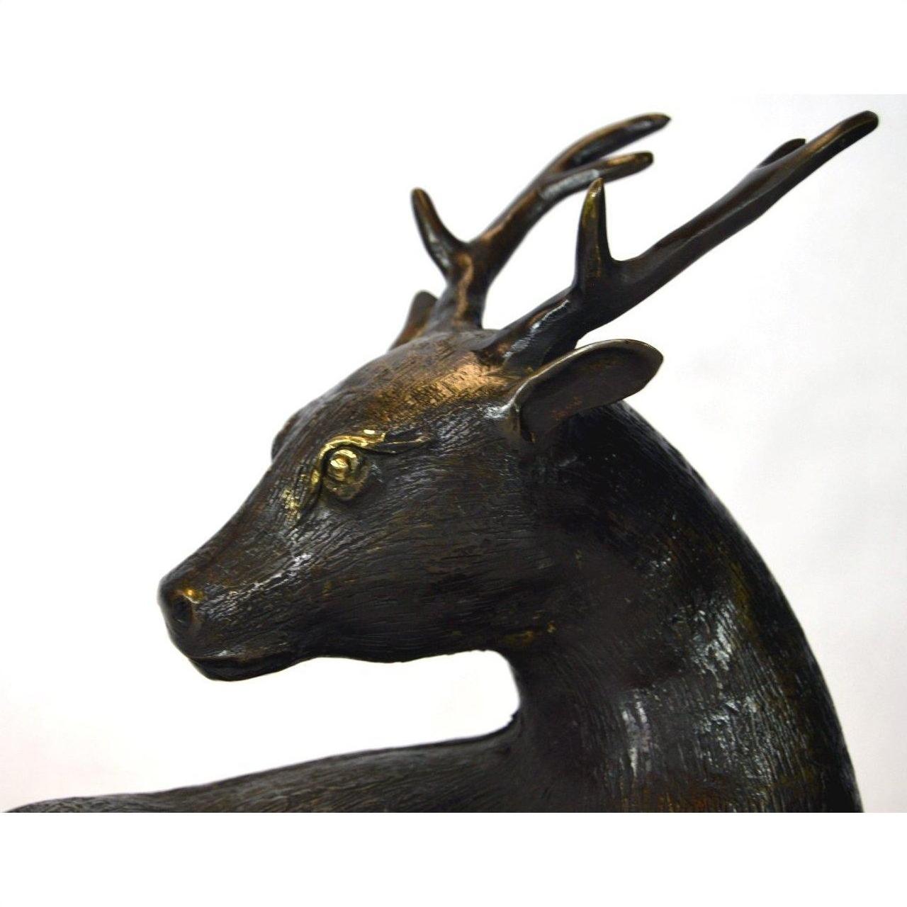Bronze sitting deer sculpture with detailed antlers and textured surface, close-up view.