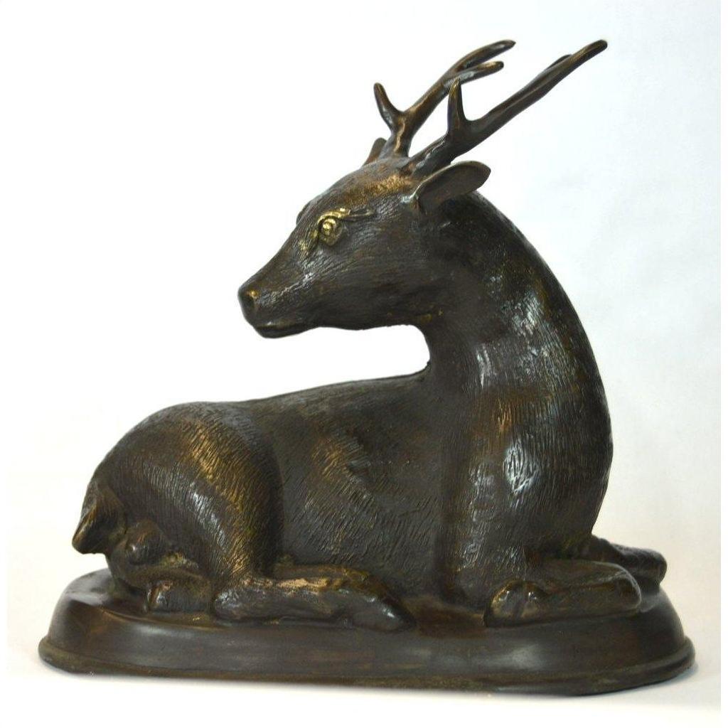 Bronze sitting deer sculpture with detailed antlers on oval base, close-up view, very good condition.