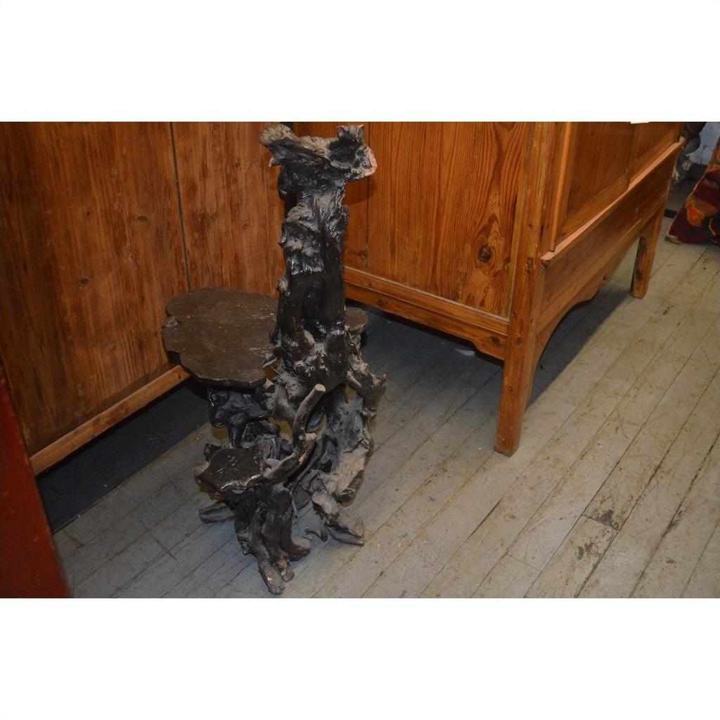 Small black wood root table with organic shape on wooden floor next to natural wood furniture, full view.