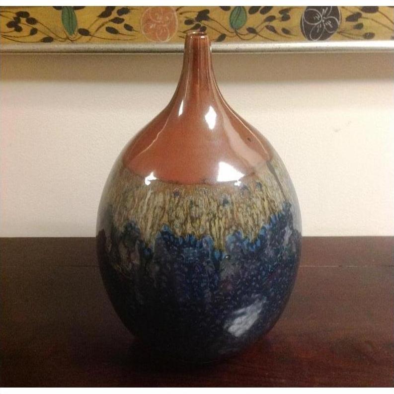 Close-up of a glossy ceramic vase with a narrow neck, featuring gradient brown-blue hues on a wooden surface.