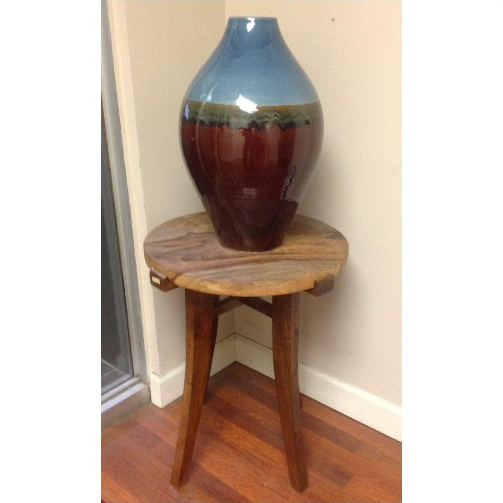 Blue and brown ceramic vase on a small round mango wood table in a corner with wood flooring.