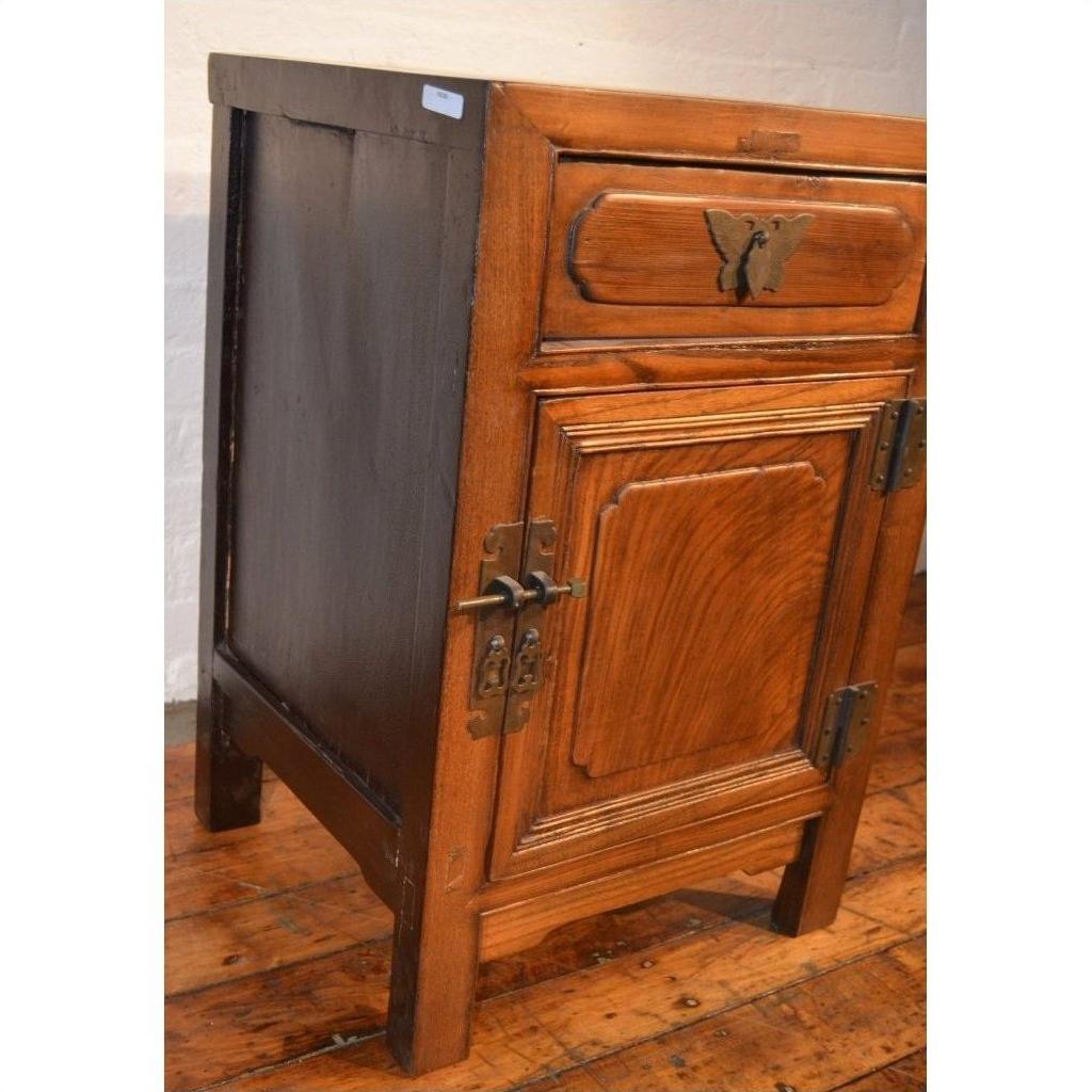 Wooden small side cabinet with drawer, door, and butterfly brass hardware on wooden floor.