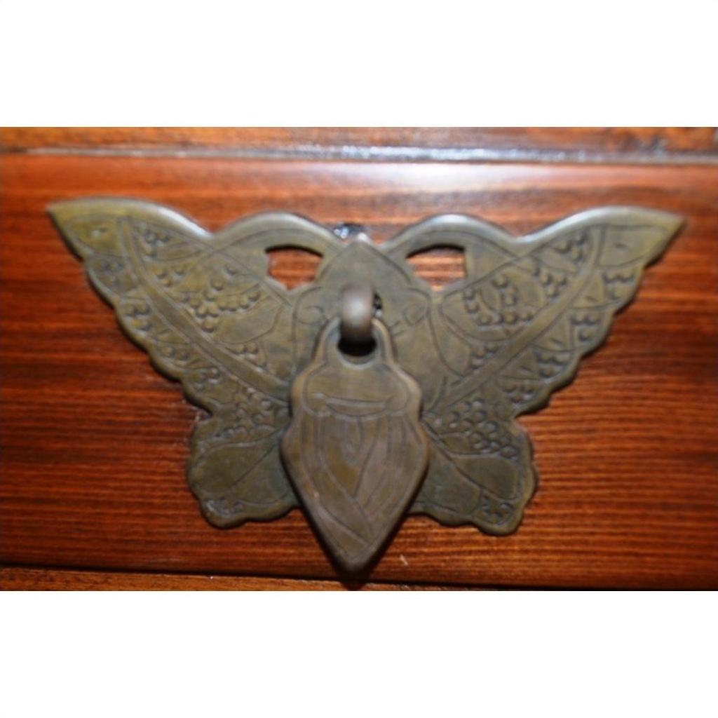 Brass butterfly-shaped drawer pull with ornate wing design on small side cabinet.