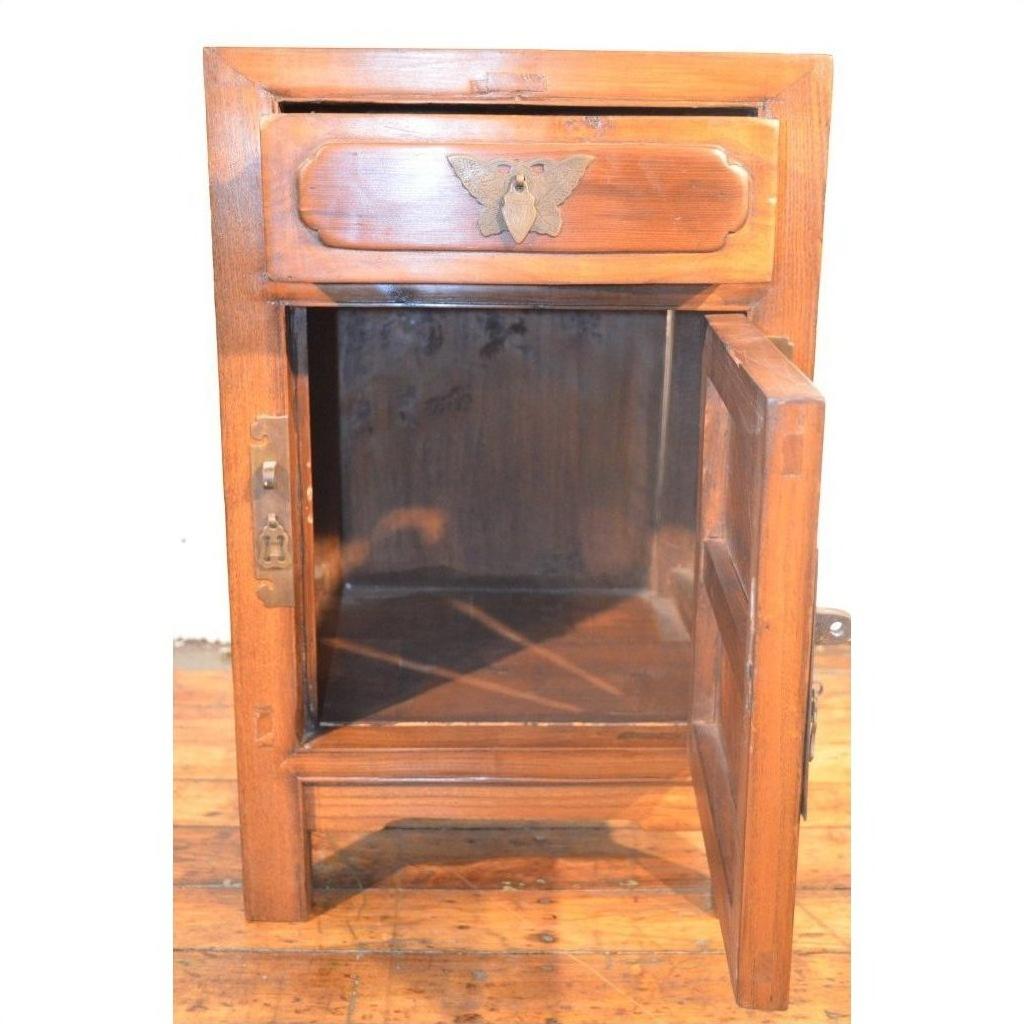 Light wood side cabinet with butterfly brass hardware on a wooden floor indoors.