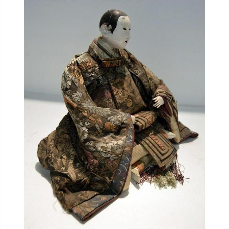 Close-up of a Taisho Samurai Doll seated with hands on lap, wearing ornate patterned robes.
