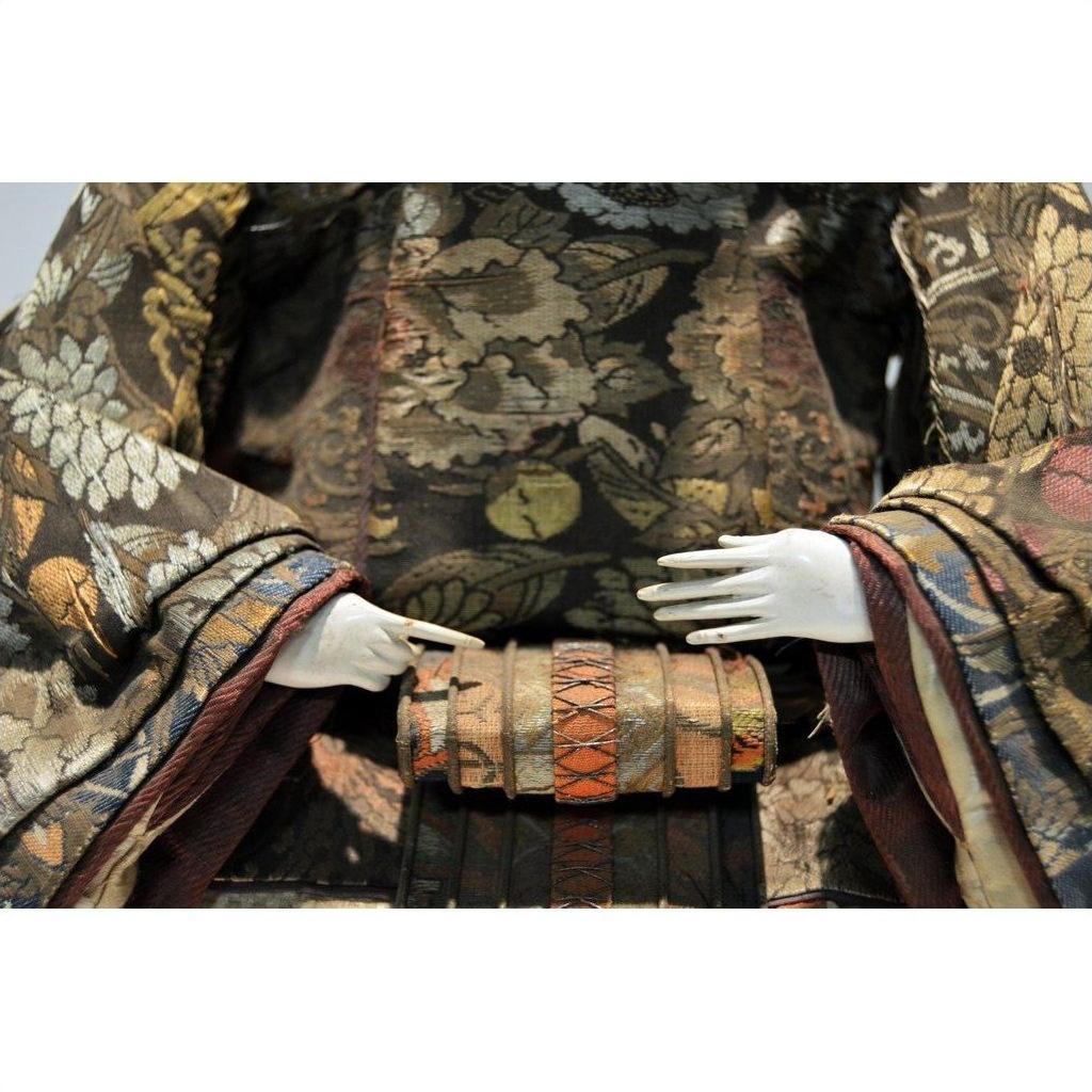 Close-up of a Taisho Samurai Doll in ornate floral-patterned fabric attire with delicate white hands.