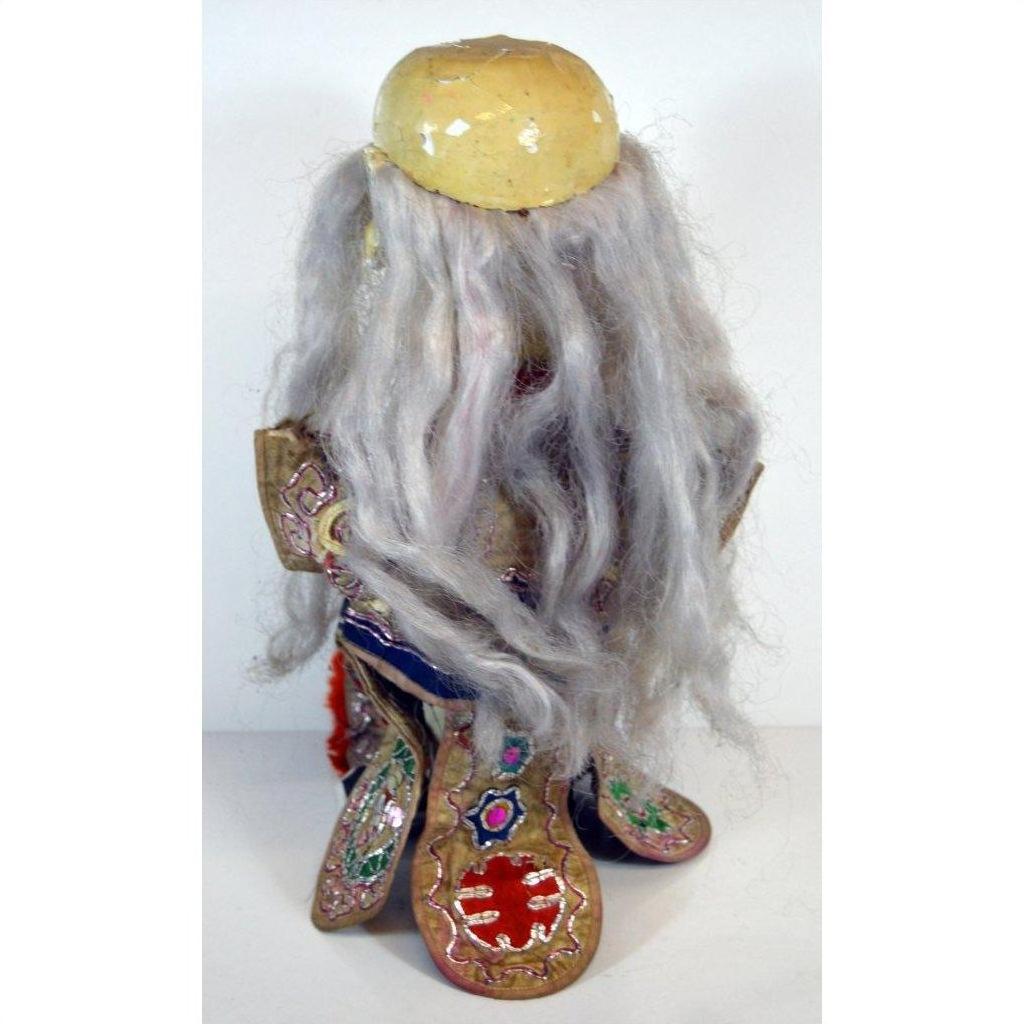 Gray-haired doll with embroidered clothing and worn beige headpiece, close-up, indoors.