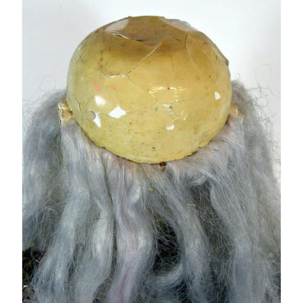 Yellowed plastic dome with cracks and long gray hair strands, vintage opera doll style, close-up.