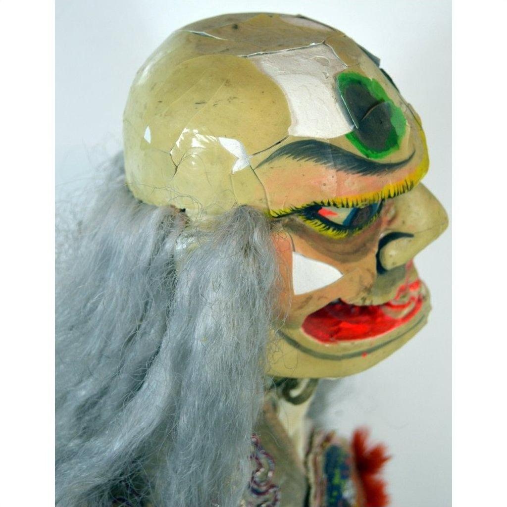 Painted ceramic mask with gray hair, bold features, and a green spot on forehead, close-up.