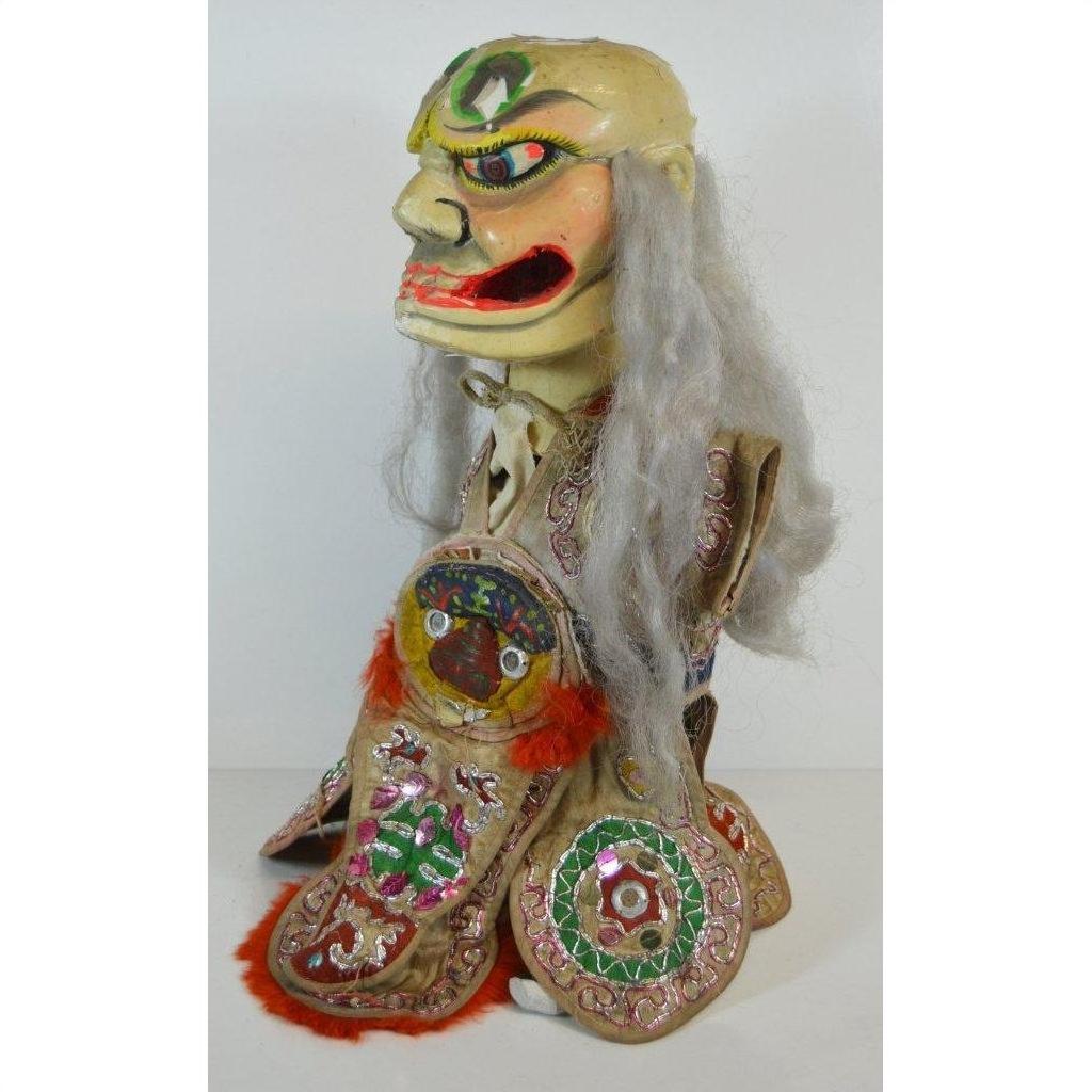 Gray-haired fabric puppet with fierce face and embroidered clothing, close-up, indoor setting.