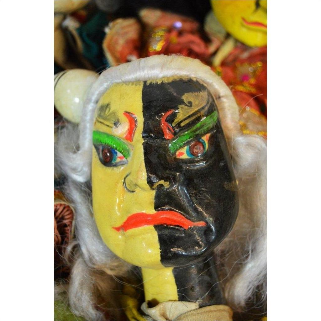 Yellow and black hand-painted mask with green brows, white hair, and red lips, ceramic close-up on plain background.