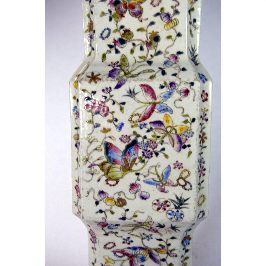 Close-up of a white porcelain tall vase with hand painted butterflies and vibrant floral designs.