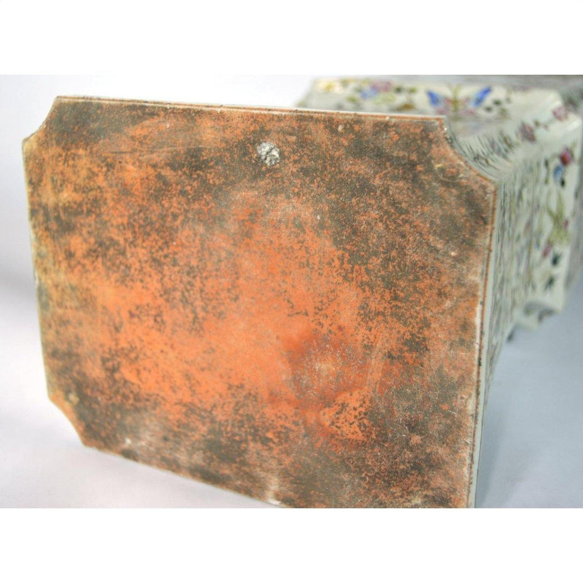 Close-up of a white porcelain vase base with hand painted butterflies and floral designs, rustic weathered finish.