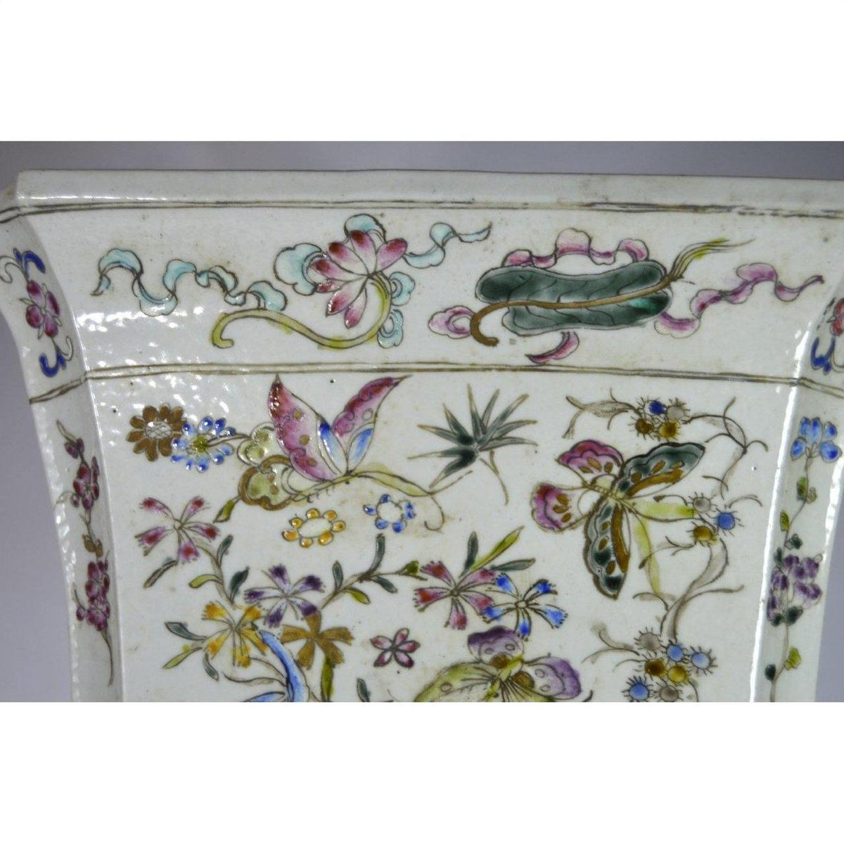 White porcelain vase with hand painted pastel flowers and butterflies, tall shape, on a plain background.