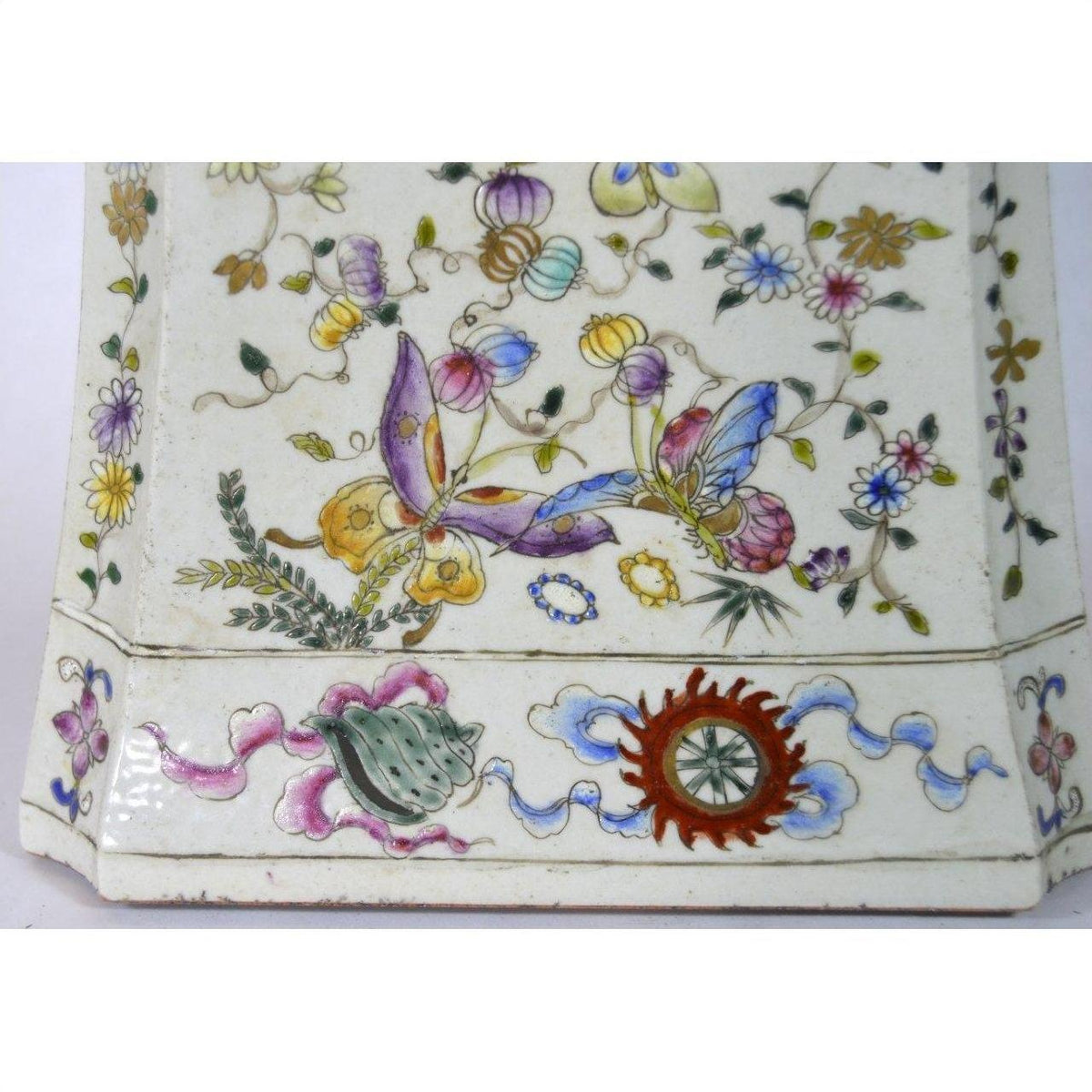 White porcelain tall vase with colorful floral and butterfly designs, red and green emblem at base, indoor setting.