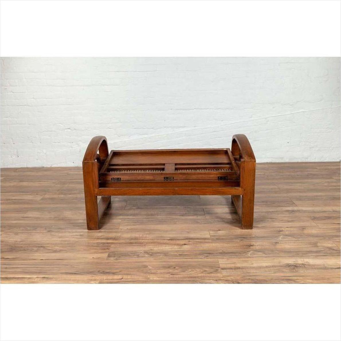 Brown wooden coffee table frame without top beside teak wood settee on wooden floor against white brick wall indoors.