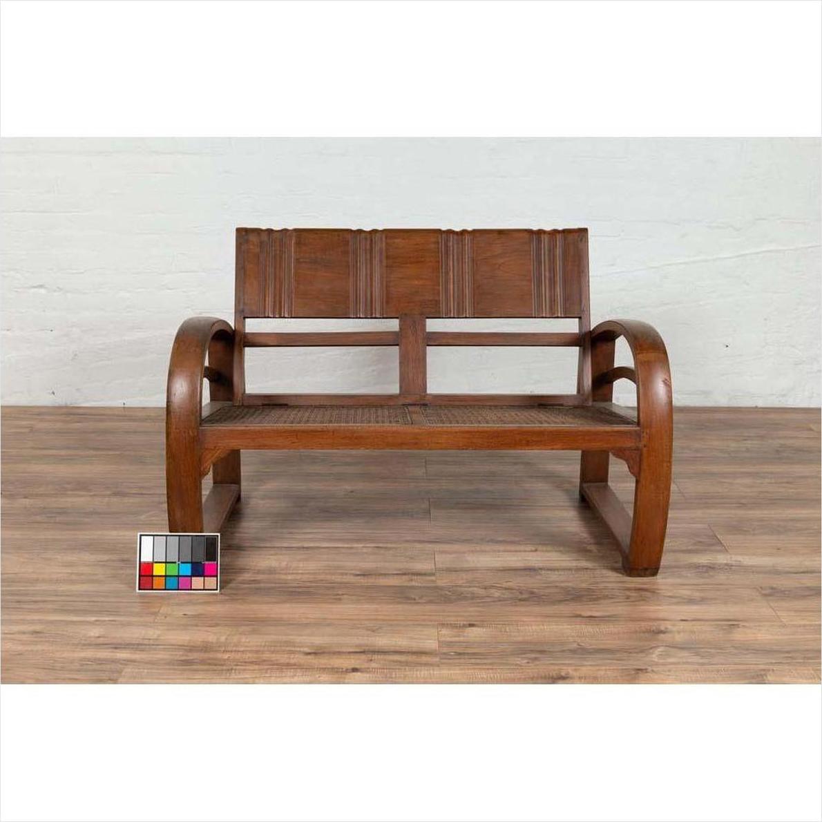 Brown teak wood settee with folding back, looping arms, and cane seat on wooden floor with color chart in front.