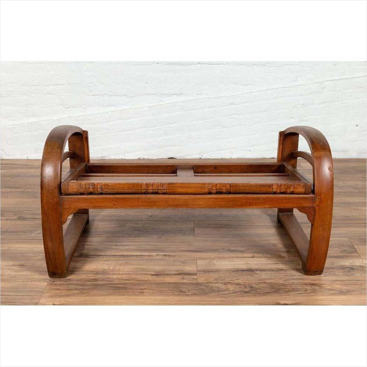 Brown wood coffee table base with curved legs next to a teak wood settee with cane seat and looping arms, indoors.