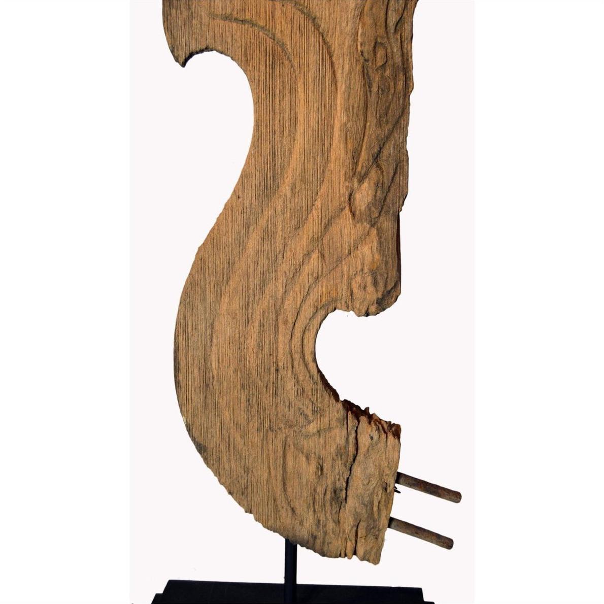 Close-up of 19th century Thai carved wood temple dragon sculpture with flowing curves on black metal base, white background.