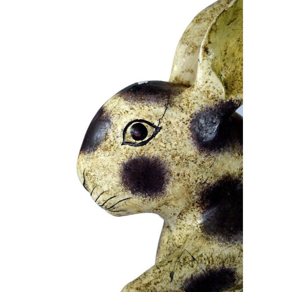 Close-up of ceramic Thai Begging Rabbit figurine with brown spots and red eye on a white background, facing left.