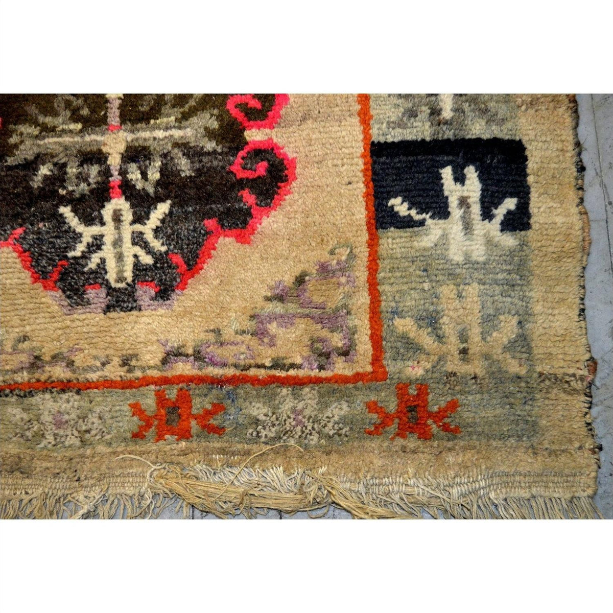 Close-up of Tibetan prayer rug corner, wool, black, red, and beige geometric pattern, fringe visible, good condition.