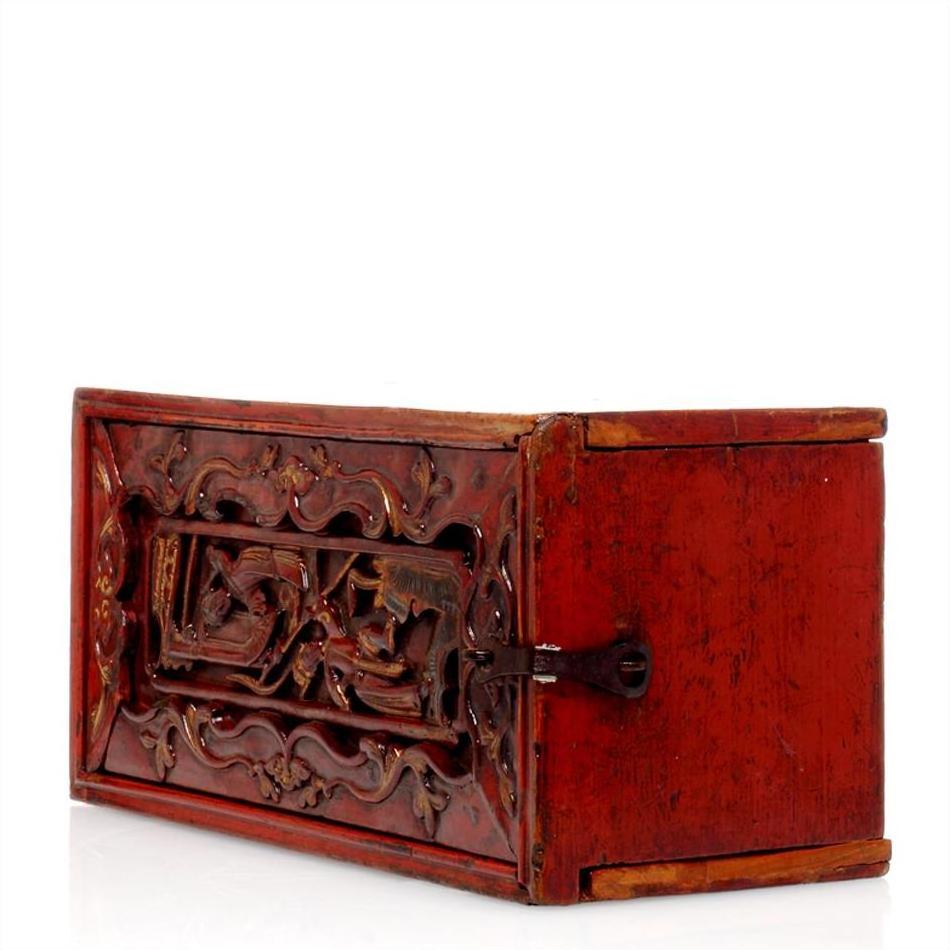 Close-up of red wooden rectangular treasure box with hand-carved raised floral pattern and metal latch on white background.