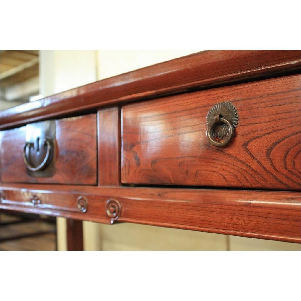 Close-up of antique elmwood triple drawer desk with bronze hardware in a bright, well-lit room.