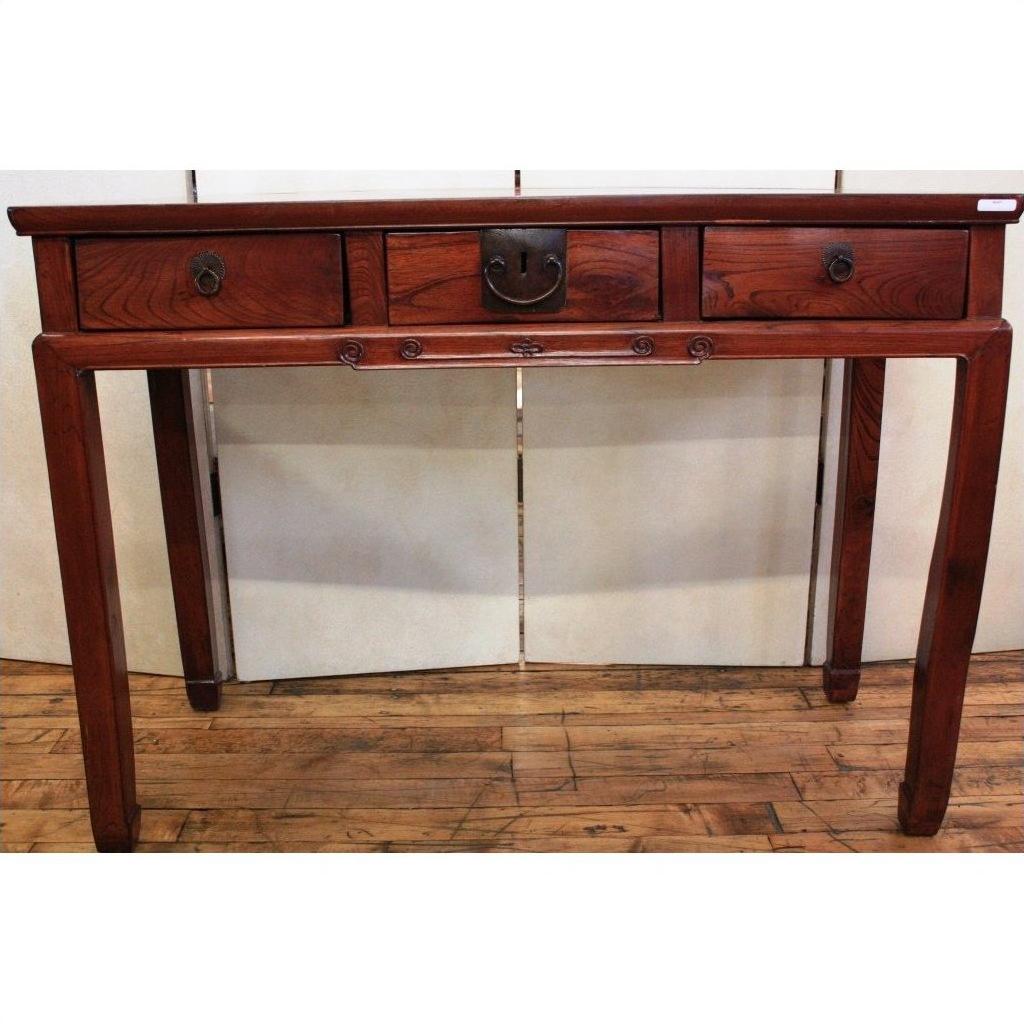 Brown wooden triple drawer desk with bronze hardware and four straight legs, shown on a wooden floor.