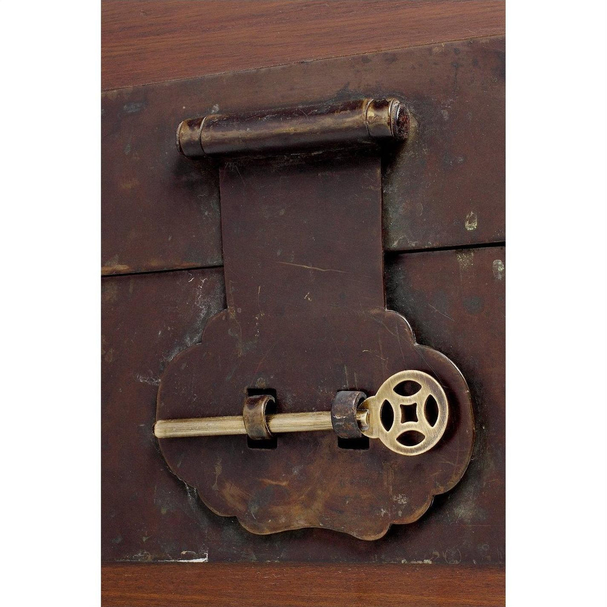 Close-up of a brass key in the lock of an old, dark natural wood trunk.