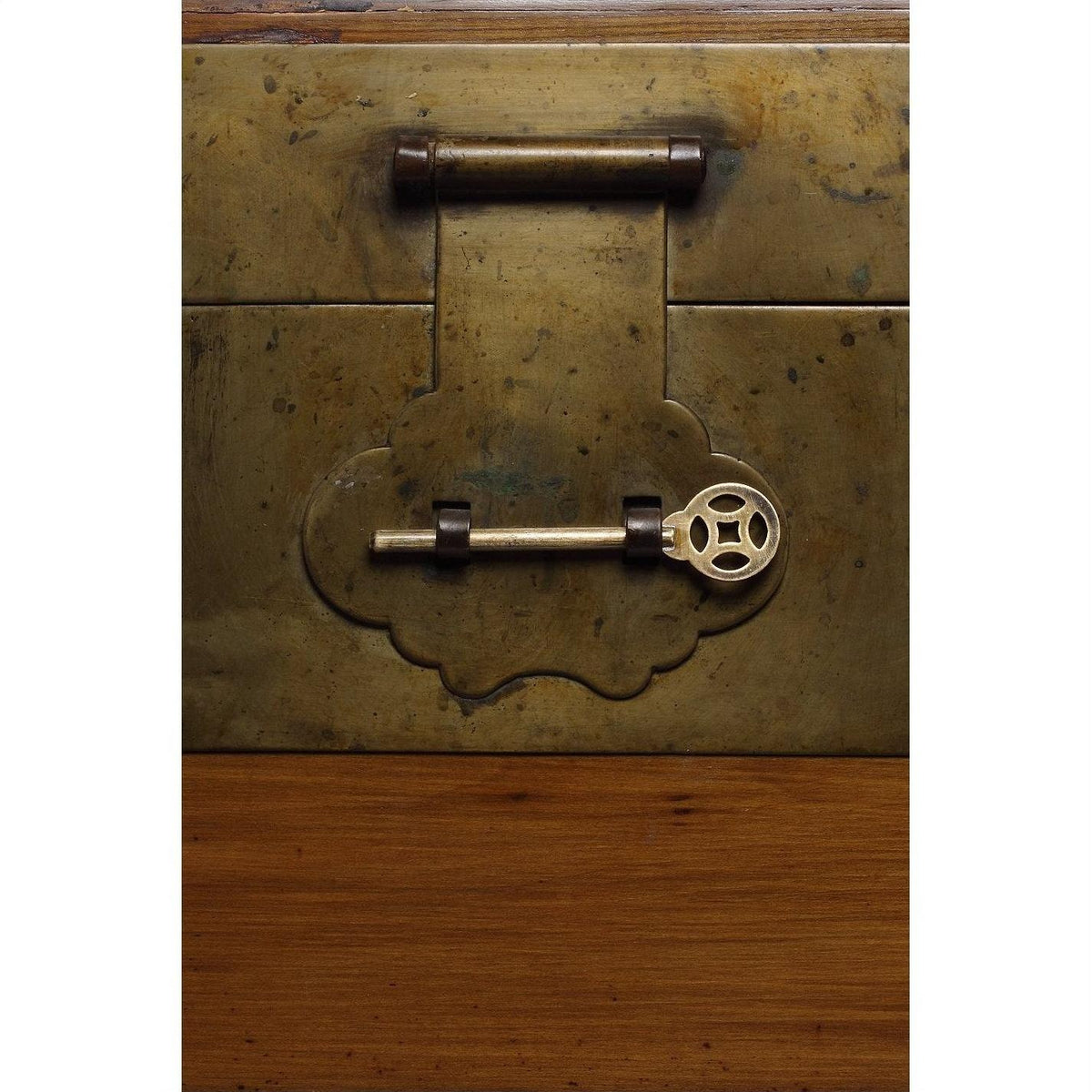 Close-up of ornate brass hardware and key on elmwood surface of Chinese trunk.