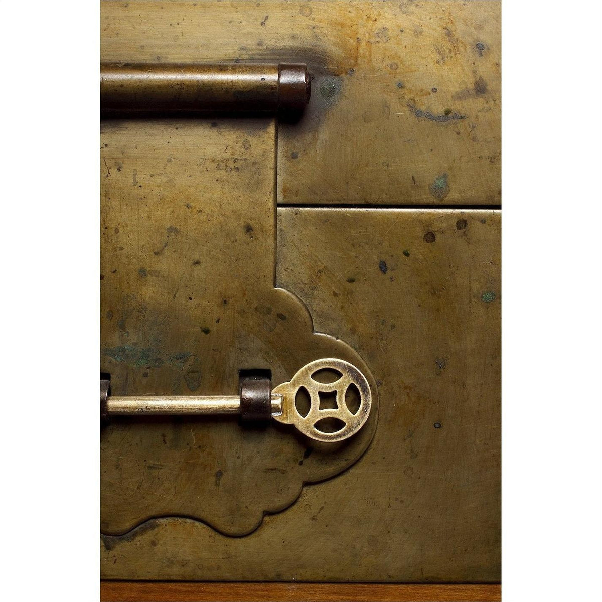 Close-up of an ornate brass key in the lock of a decorative-edged trunk.