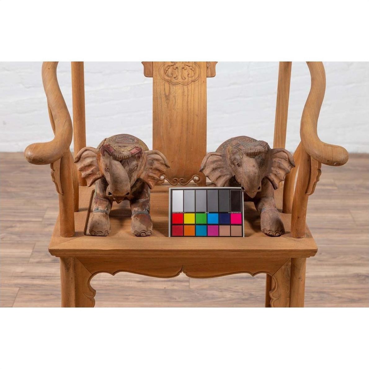 Close-up of two painted wooden elephant sculptures from Chiang Mai on a wooden chair with a color chart.