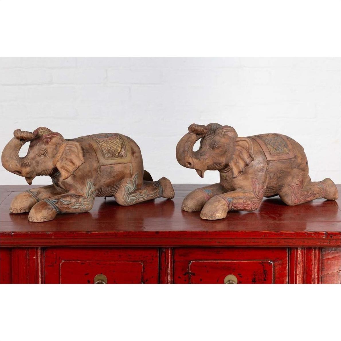 Close-up of two vintage Thai carved and painted elephant sculptures on a red wooden cabinet in Chiang Mai style.