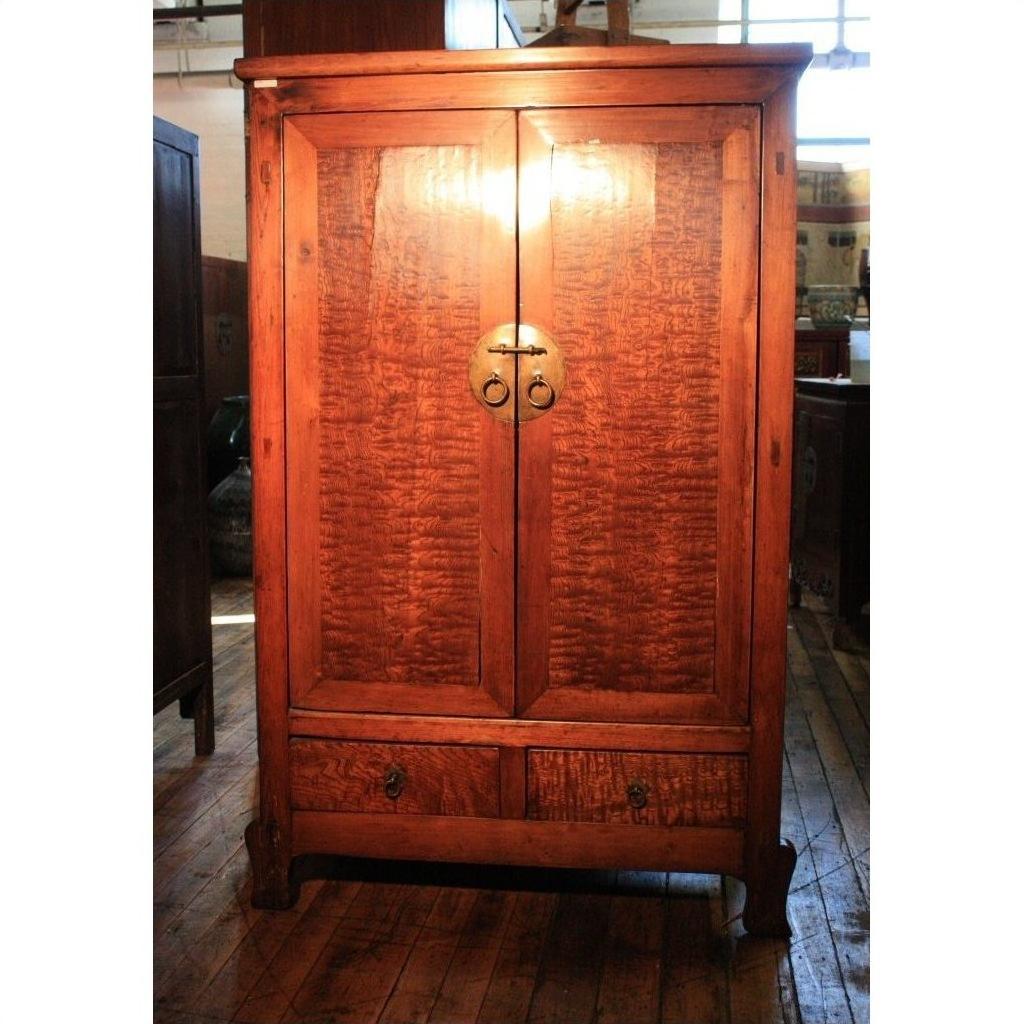 Brown burl wood cabinet with double doors, brass handle, and bottom drawer on a wooden floor.