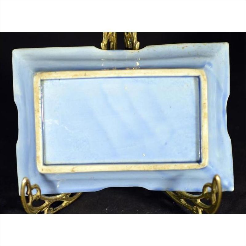 Close-up of blue and white hand painted porcelain dish with raised border, displayed on ornate golden stand.