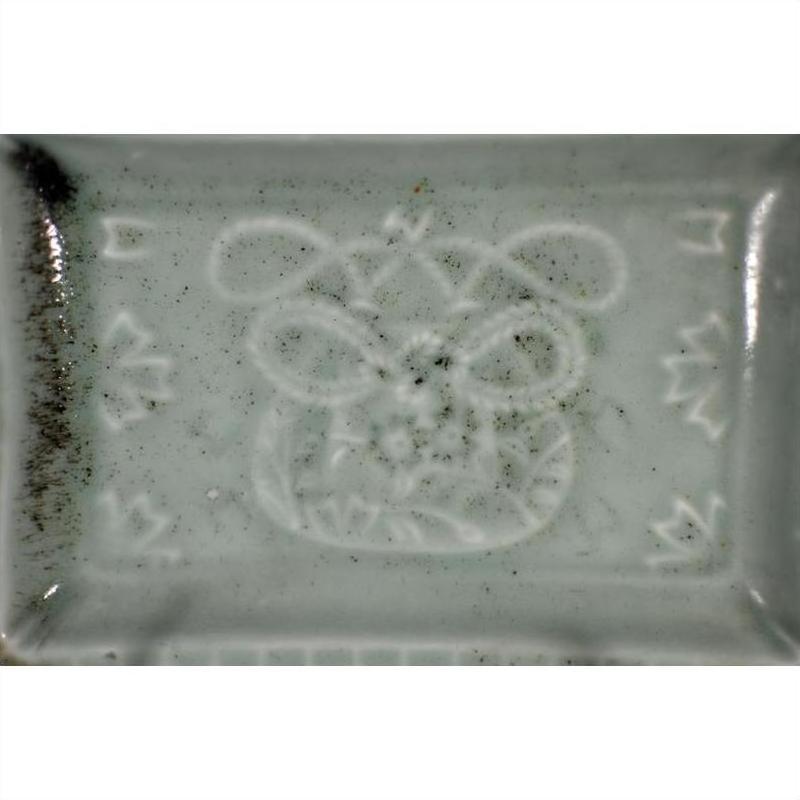 White porcelain dish with hand painted abstract animal face, geometric designs, and dark stains on left edge, close-up.
