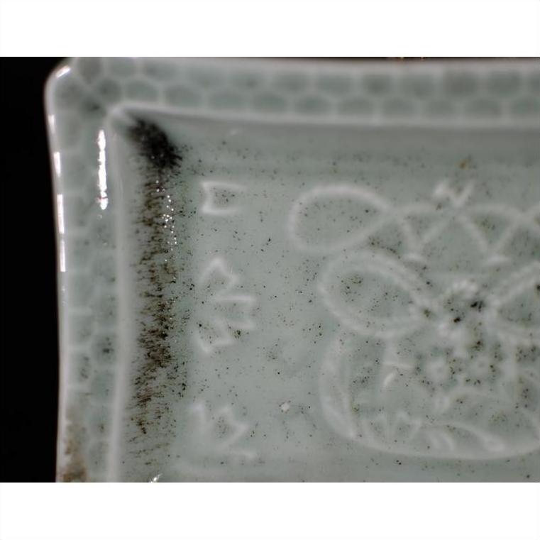 Close-up of a white porcelain dish with hand painted geometric border, black specks, and subtle patterns.