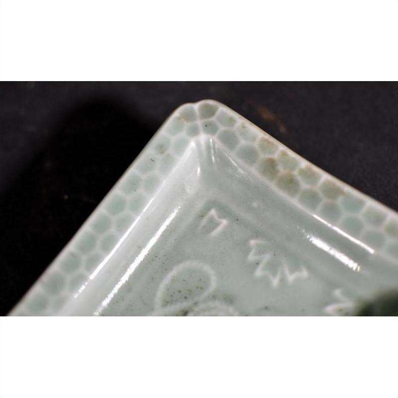 Close-up of light green porcelain dish with engraved rim and hand painted Asian honeycomb pattern.