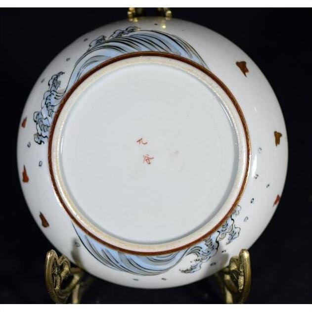 Close-up of base of vintage Asian porcelain plate with blue wave pattern, brown fish, and red Chinese characters at center.