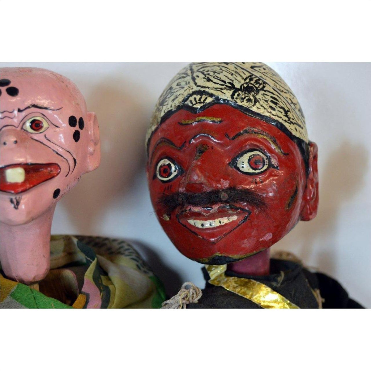 Close-up of two vintage Balinese puppets, one pink and one red, with painted clothing and decorative headgear.
