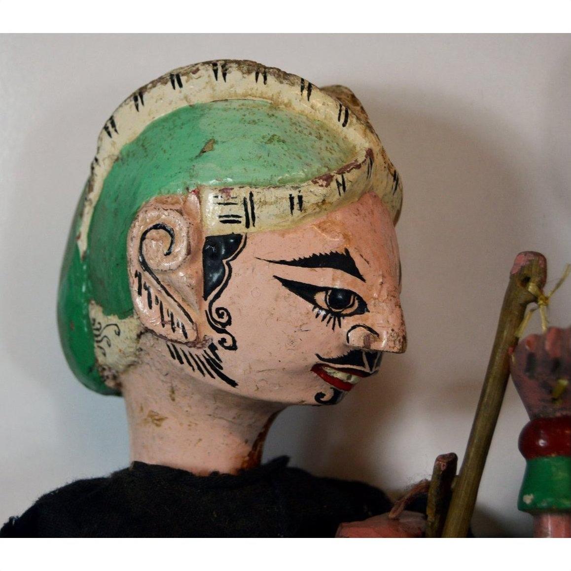 Side view of vintage Balinese puppet with green hair, black face designs, holding a stick.