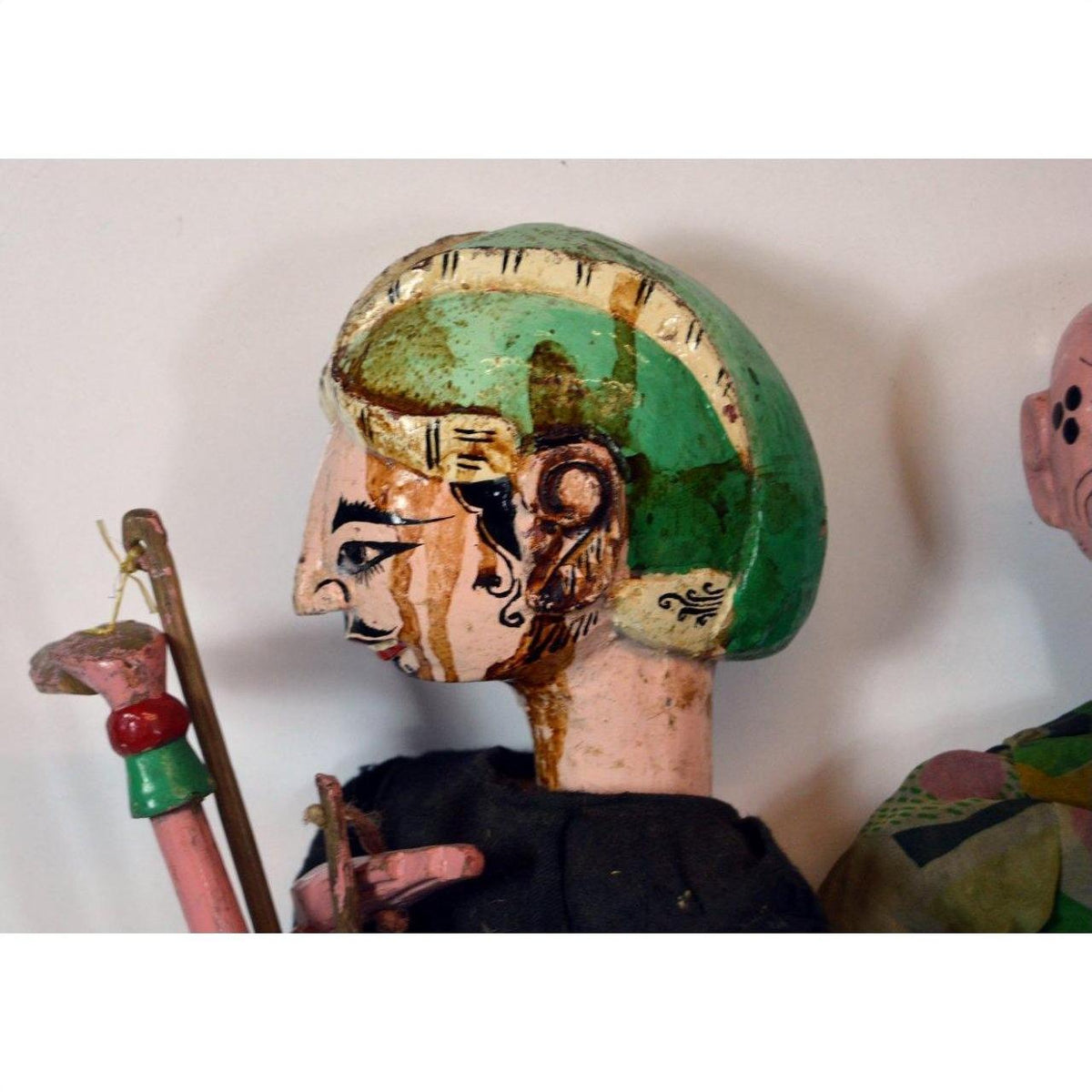 Close-up of vintage Balinese puppet in painted wood with green headpiece and black clothing, side profile view.