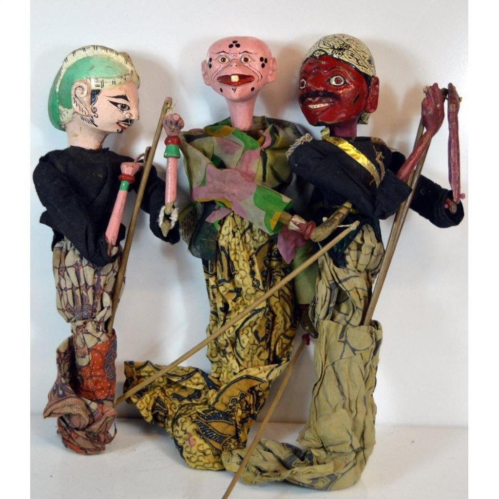 Close-up of three colorful vintage Balinese puppets in patterned clothing, wood material visible, grouped together.