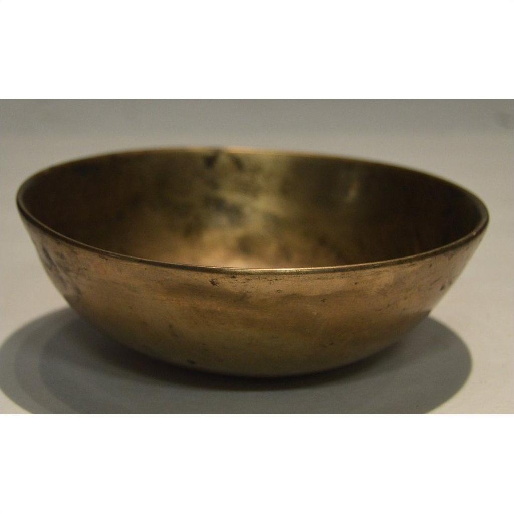 Vintage brass offering bowl with slightly uneven surface on a light background, close-up view.
