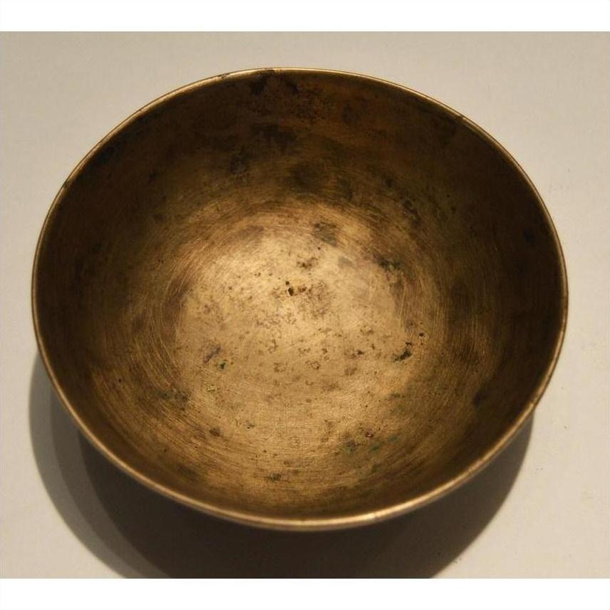 Brass offering bowl with weathered, tarnished surface on light background.