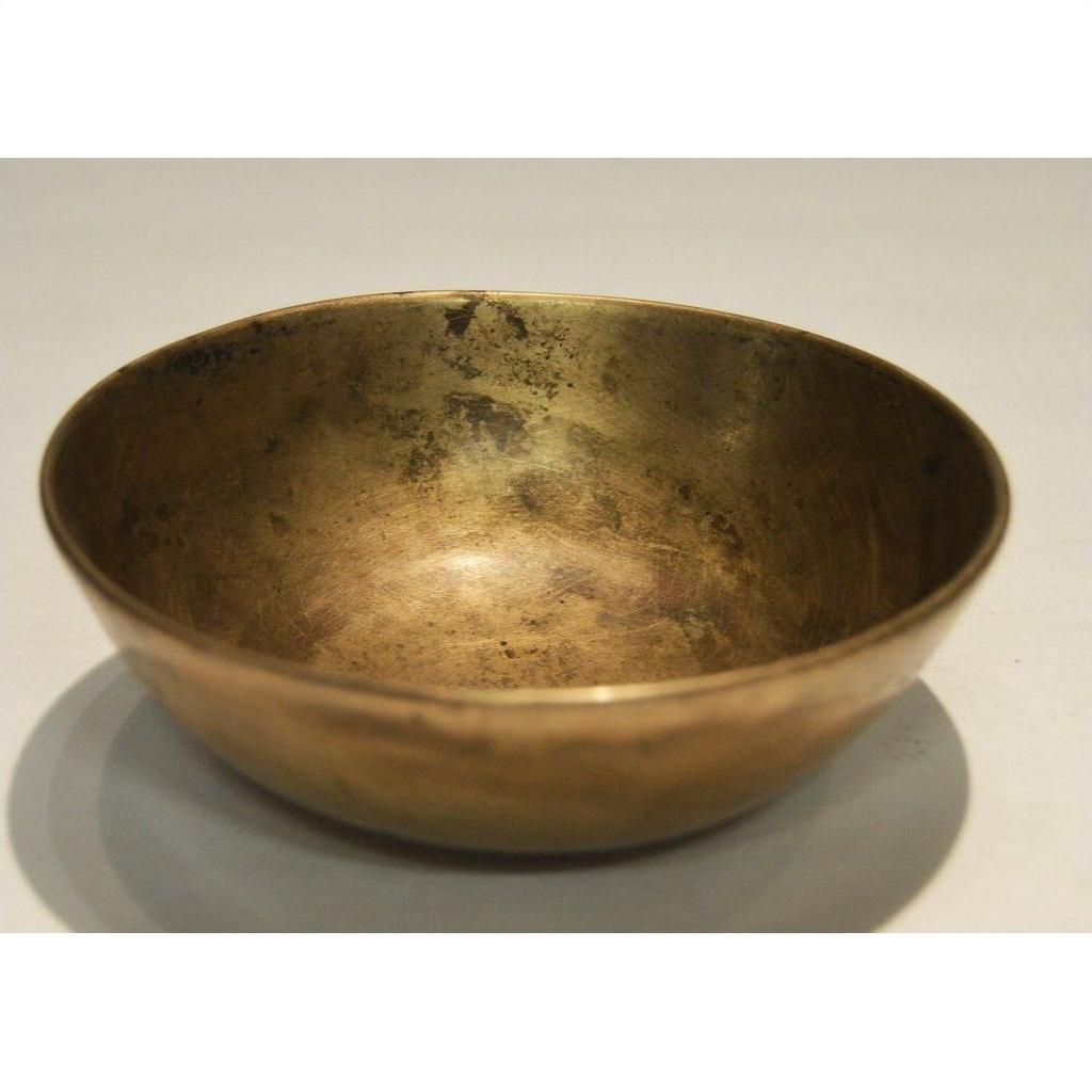 Brass offering bowl with vintage finish on a simple, light-colored surface, close-up view.
