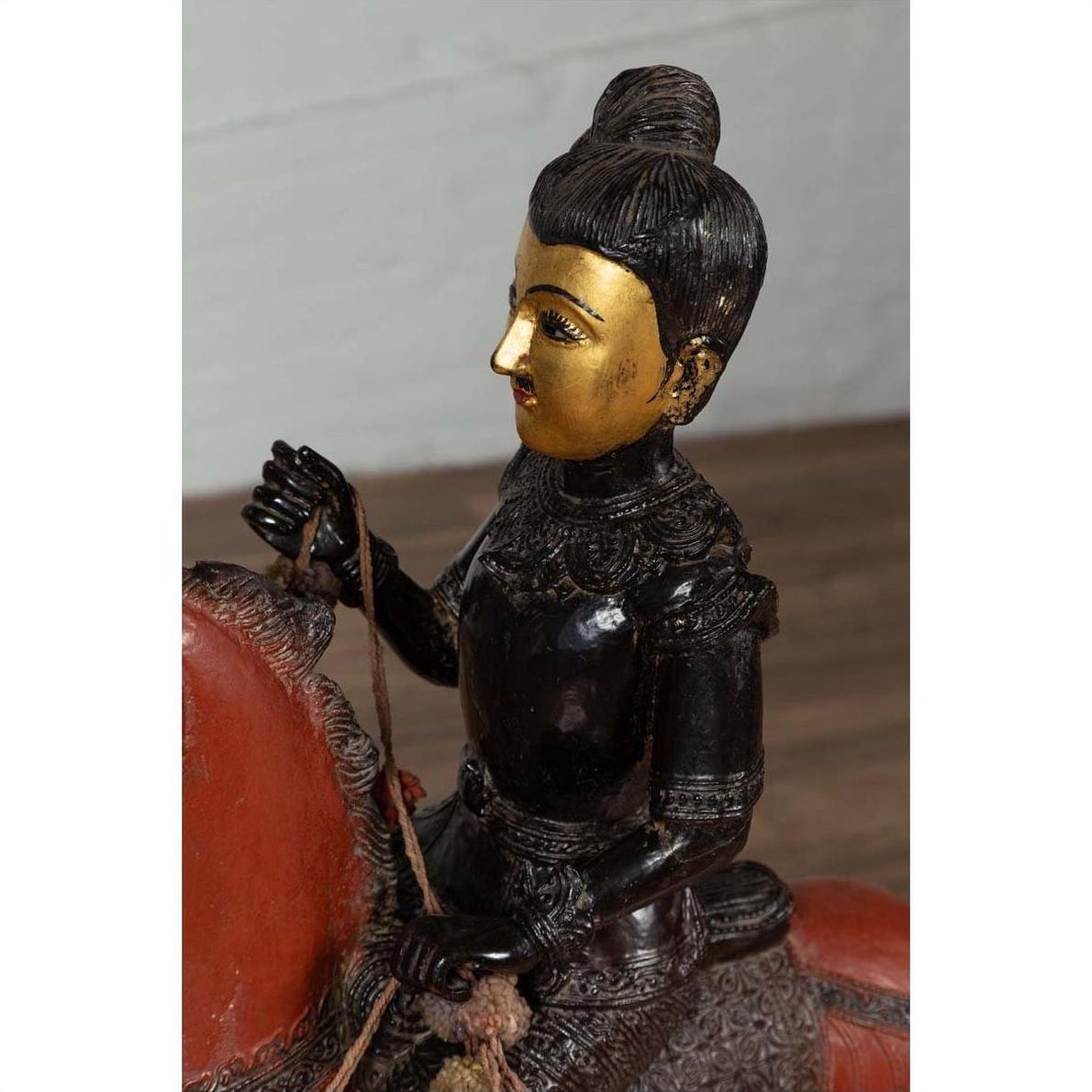 Close-up of black polychrome wooden Burmese warrior statue riding a red horse with gold-painted face.